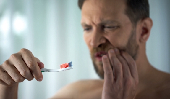 Man in pain holding cheek with blood on toothbrush